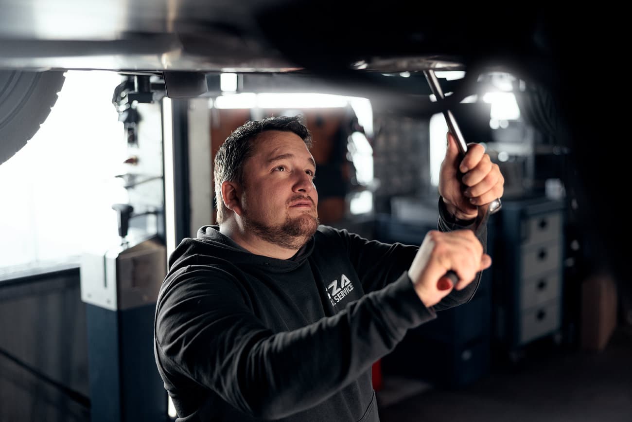 Mechaniker von RZA-KFZ Service arbeitet mit Werkzeug unter einem Fahrzeug auf der Hebebühne